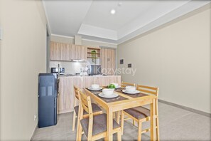 A compact kitchen with wooden cabinets, a refrigerator, and a dining area with a table set for four. - Kiyo by Kozystay - Kemayoran (Jakarta)