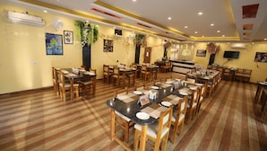 A spacious dining area with multiple tables and chairs, air conditioning units, and decorative plants.