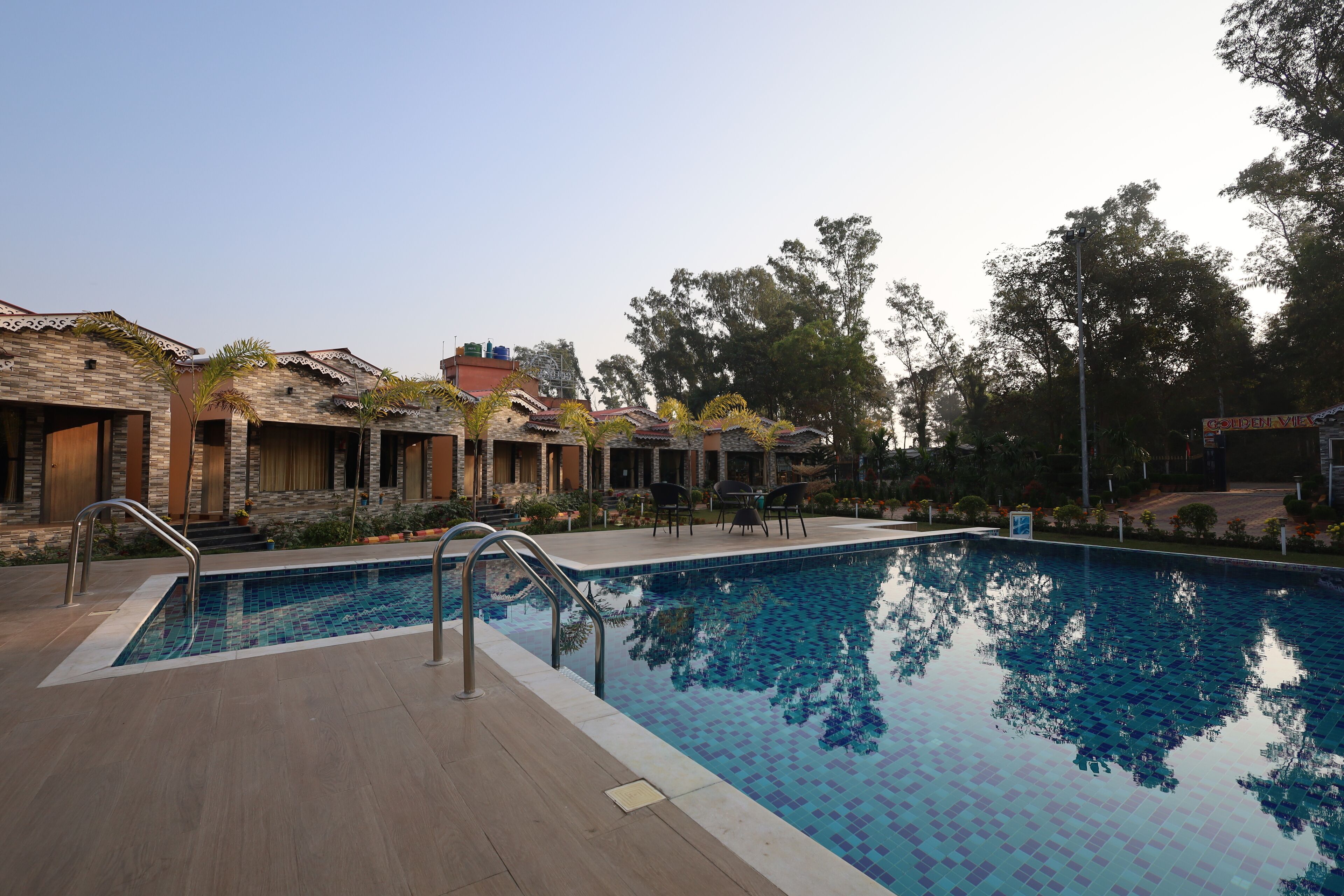 A swimming pool with a tiled deck, surrounded by buildings with stone facades and a clear sky.