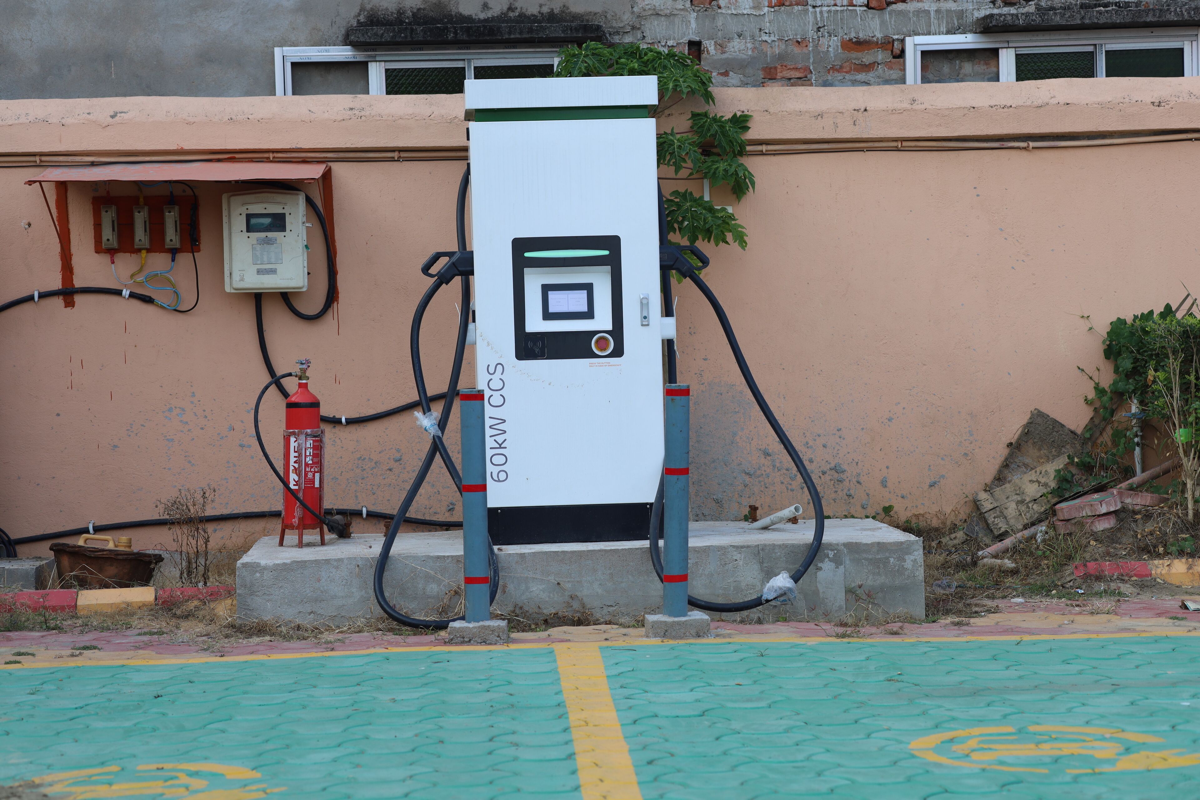 A 60kW CCS electric vehicle charging station with a control panel, connected to a wall-mounted electrical box and hoses.