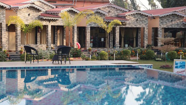 A pool area with a clear reflection, a building with a tiled roof, and outdoor seating.