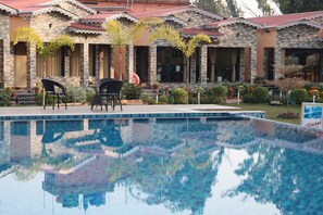 A pool area with a clear reflection, a building with a tiled roof, and outdoor seating. - Golden View Resort & Restaurant (Kanthi)