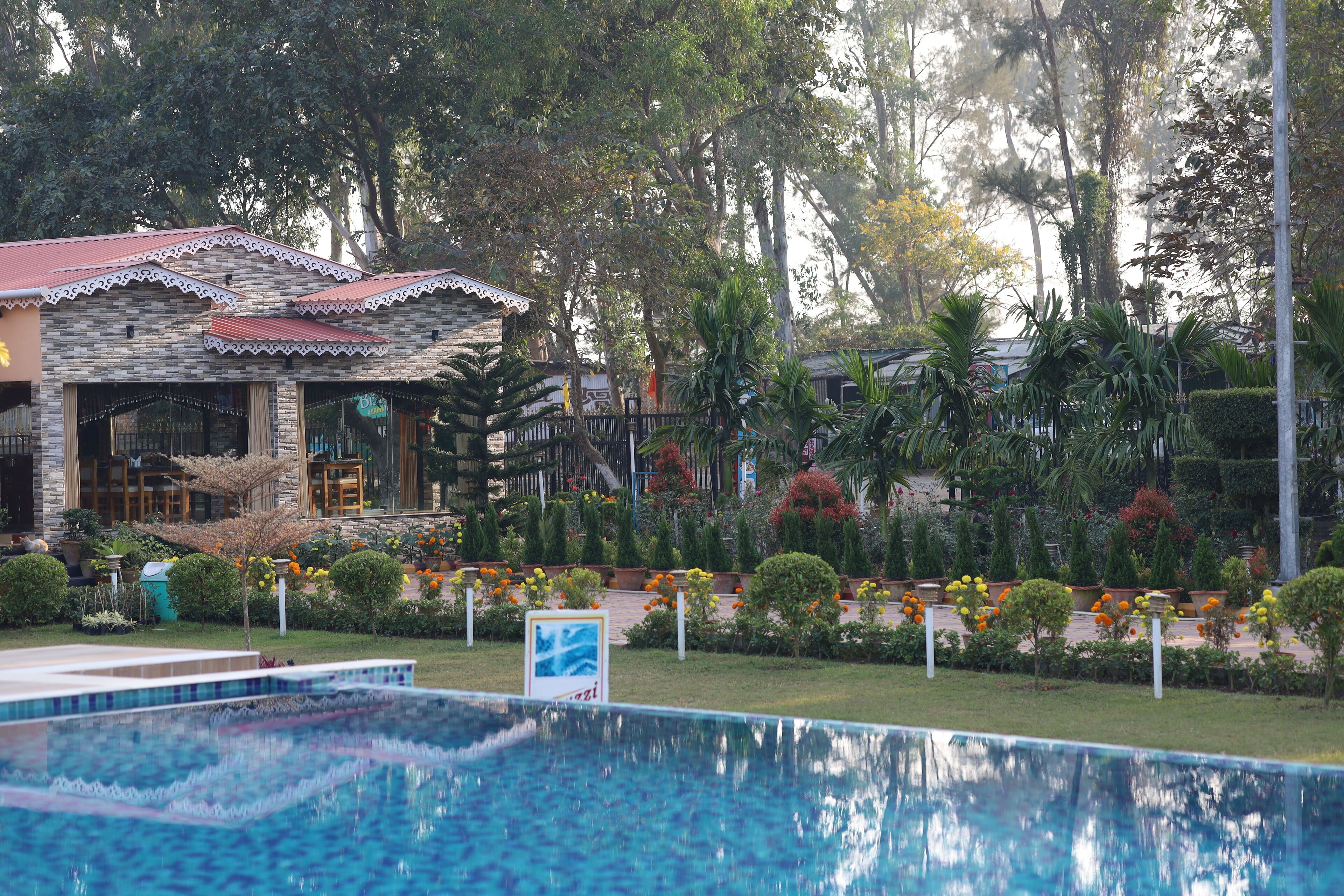 A pool area with a stone building, surrounded by well-maintained gardens and trees.