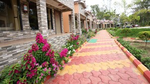 A row of stone buildings with a tiled walkway and flower beds.
