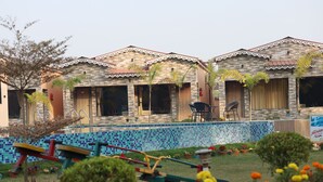A row of rooms with a tiled pool in the foreground.