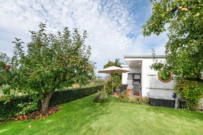 A modern house with a well-maintained garden, a patio with outdoor furniture, and a clear view of the sky.