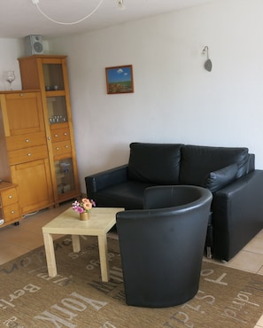A living room with a black leather sofa, a wooden cabinet, and a small table with a vase of flowers. - Holiday Home 'Seeblick' with Lake View, Private Terrace and Private Garden (Leezen)