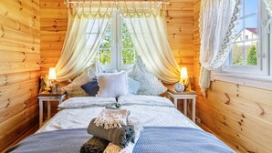 A wooden cabin bedroom with a bed, curtains, a lamp, and a window. - Premium Chalet 'Finia' with Private Terrace, Garden, and Wi-Fi (Sauldorf)