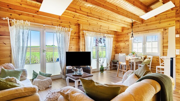 A wooden cabin interior with a sofa, TV, dining table, and large windows. - Premium Chalet 'Finia' with Private Terrace, Garden, and Wi-Fi (Sauldorf)