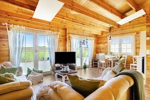 A wooden cabin interior with a sofa, TV, dining table, and large windows. - Premium Chalet 'Finia' with Private Terrace, Garden, and Wi-Fi (Sauldorf)