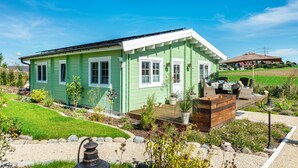 A green house with a deck, surrounded by a garden with various plants and a gravel path. - Premium Chalet 'Finia' with Private Terrace, Garden, and Wi-Fi (Sauldorf)