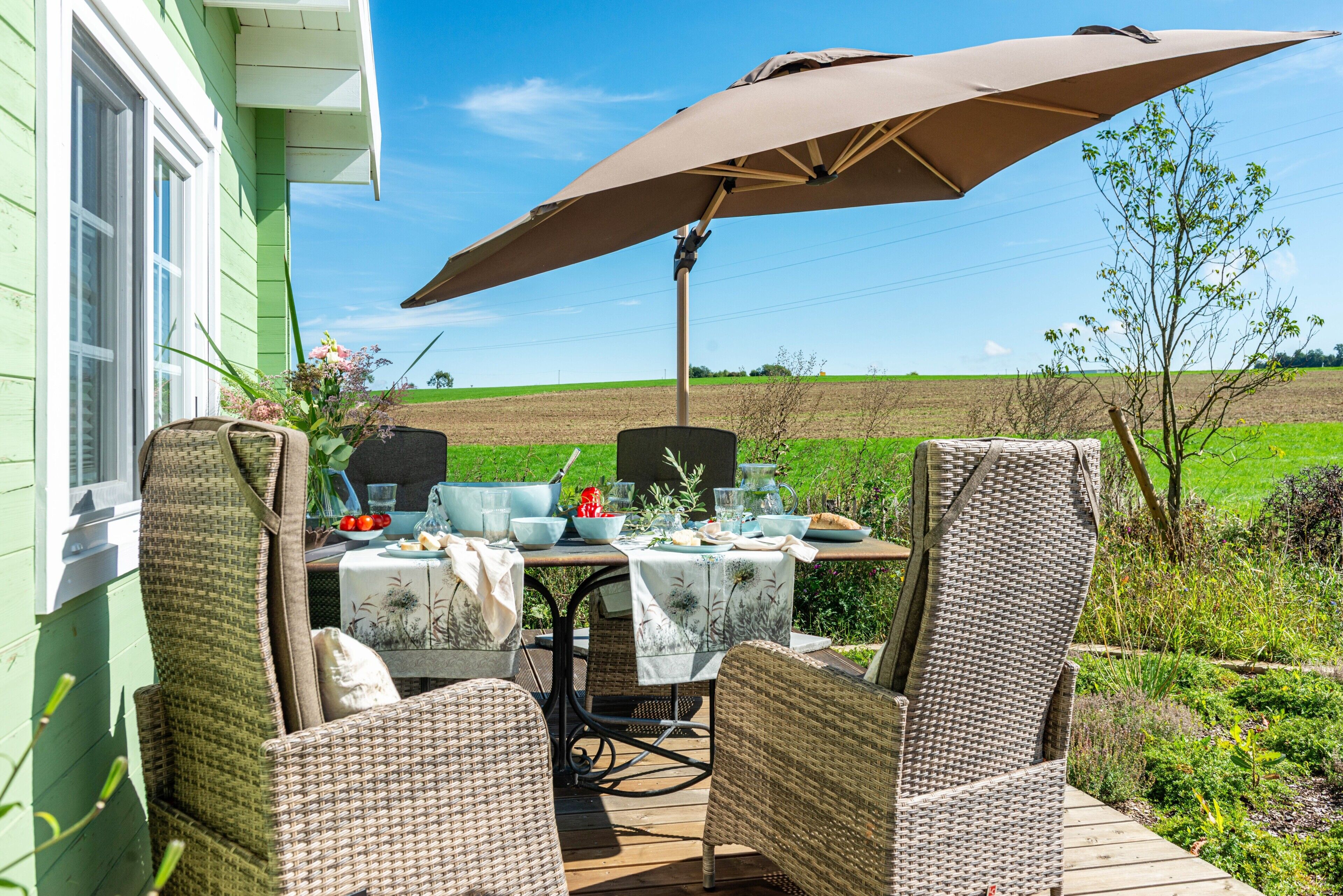 Une terrasse extérieure aménagée avec des meubles en osier, une table dressée et un grand parasol.