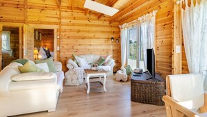 A log cabin interior with a sofa, a small table, a wicker chair, and a television. - Premium Chalet 'Finia' with Private Terrace, Garden, and Wi-Fi (Sauldorf)
