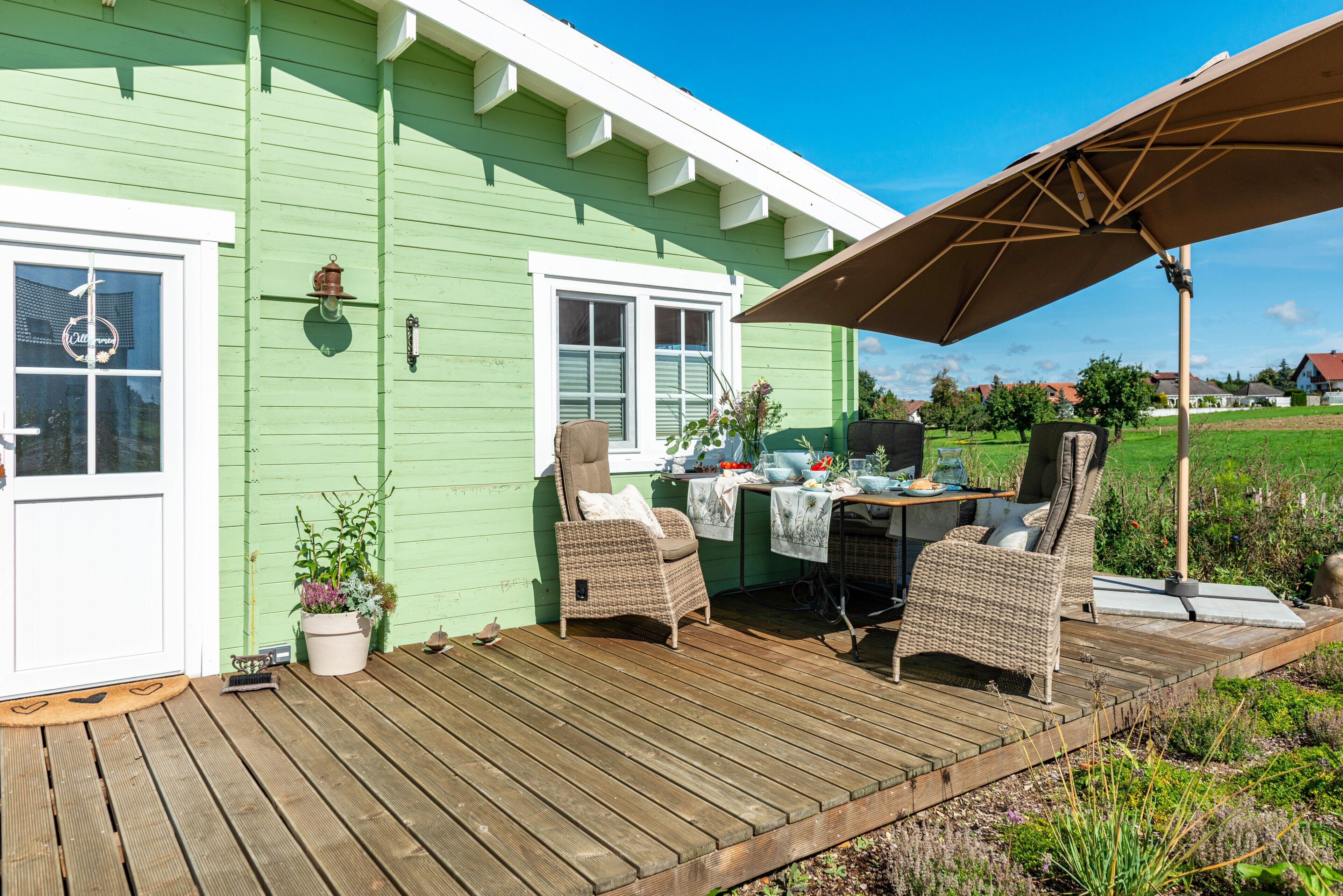Ein grünes Haus mit einer Holzterrasse, Sitzgelegenheiten und einem Tisch.