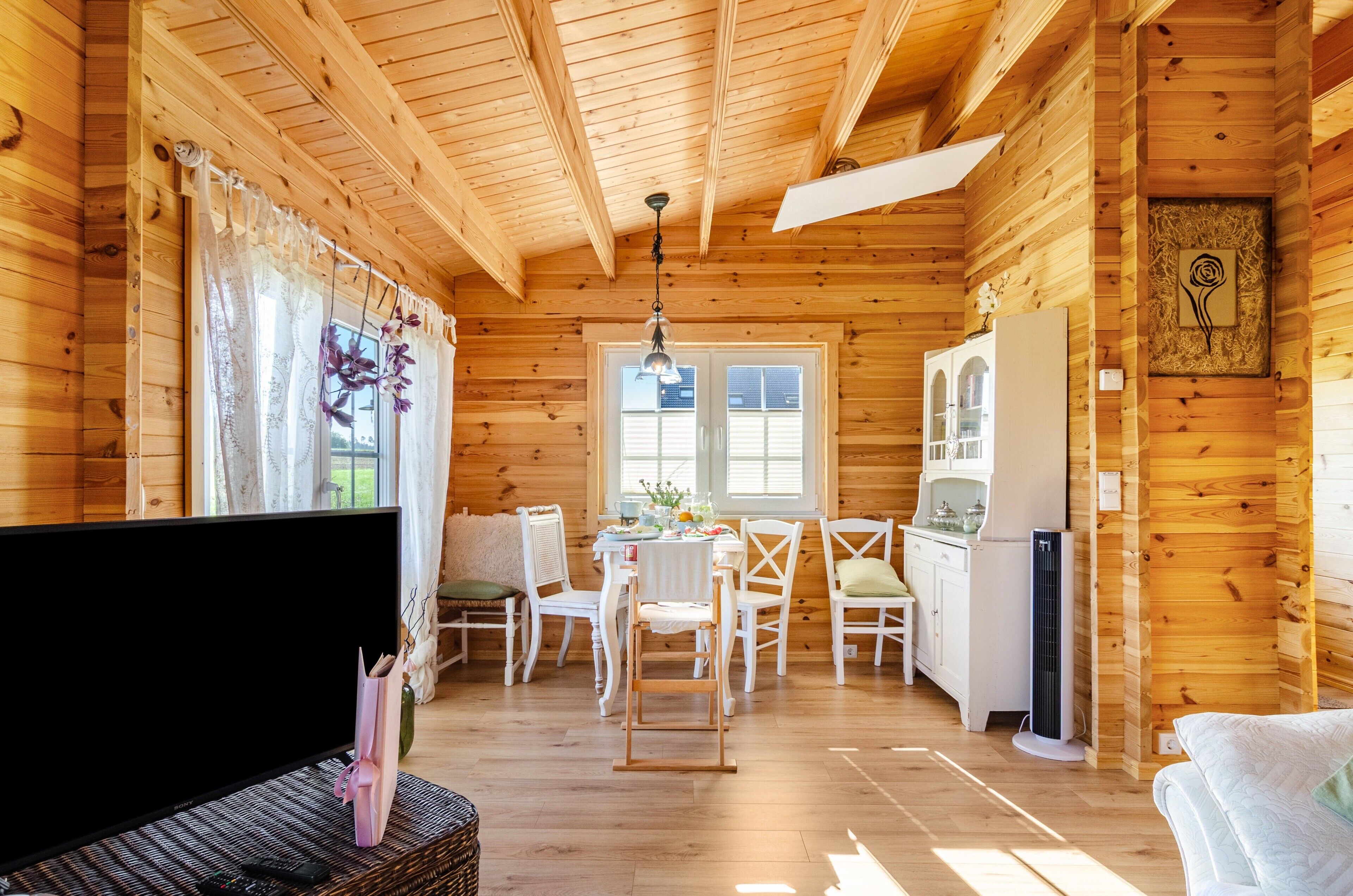A wooden cabin interior with a dining area, kitchen, and a television.