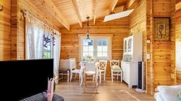 A wooden cabin interior with a dining area, kitchen, and a television.