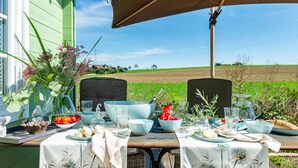 An outdoor dining area with a table set for two, surrounded by a green house and a field. - Premium Chalet 'Finia' with Private Terrace, Garden, and Wi-Fi (Sauldorf)