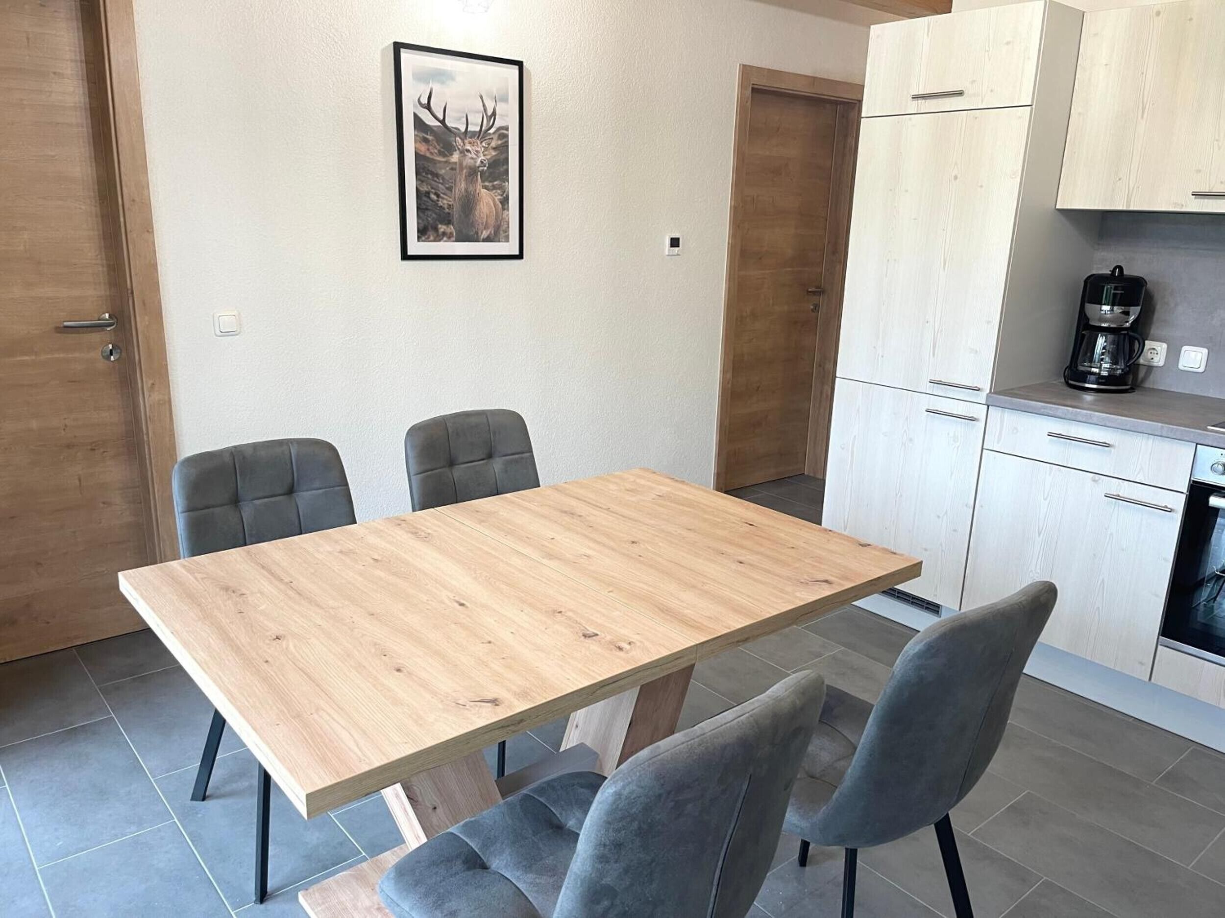 Een moderne keuken met witte kasten, een koffiezetapparaat en een eethoek met een houten tafel en grijze stoelen.