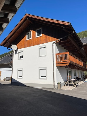 Ein zweistöckiges Gebäude mit einem Holzbalkon, einer Satellitenschüssel und einer überdachten Außenbereich-Sitzgruppe.