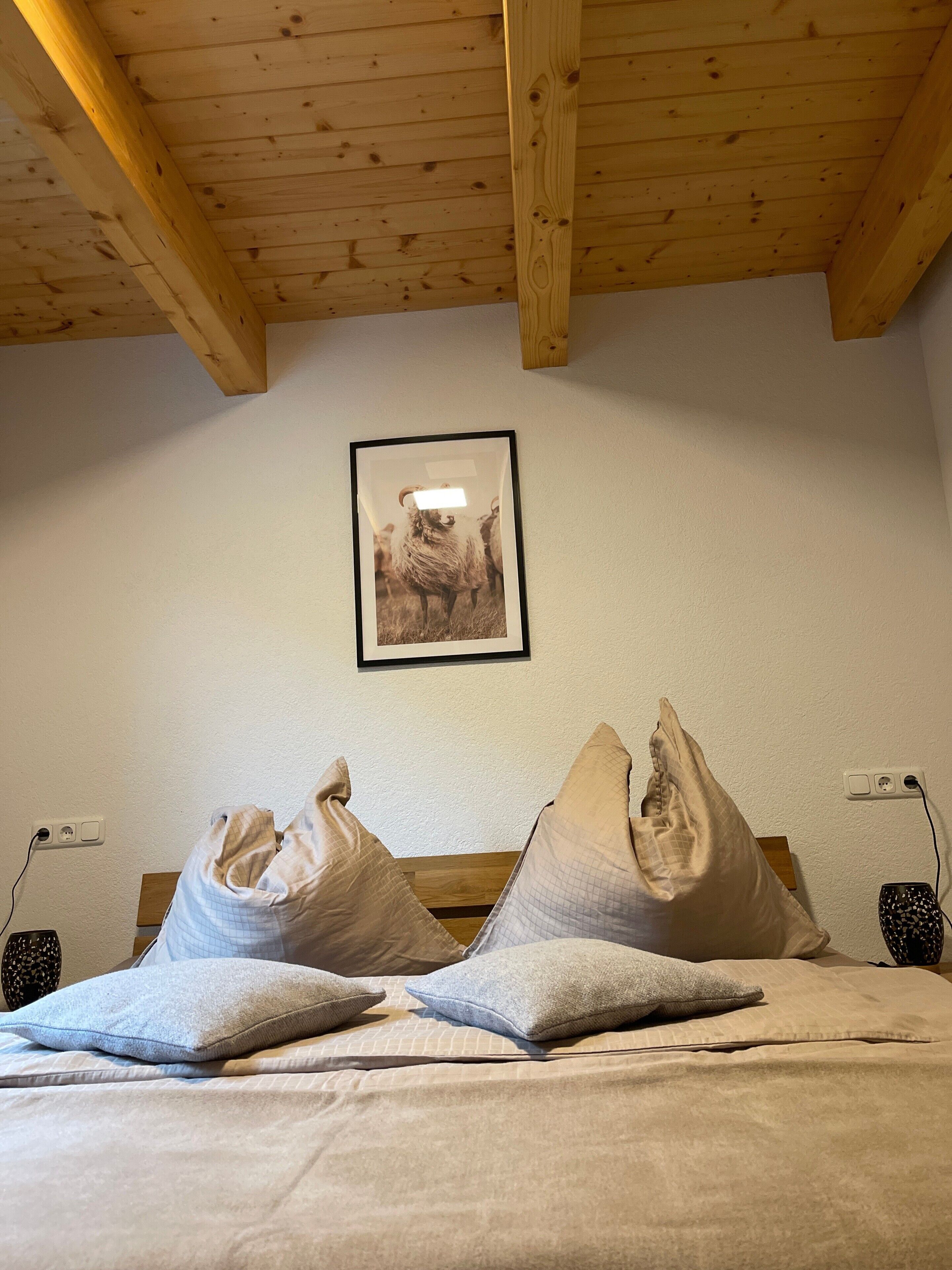 A bedroom with a wooden ceiling, a framed picture on the wall, and a bed with multiple pillows.