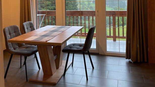 A room with a wooden ceiling, a large table with chairs, and a view of a balcony with a wooden railing.