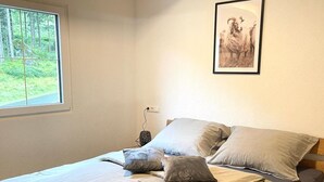A bedroom with a wooden bed frame, a window with a view of trees, and a framed picture on the wall.