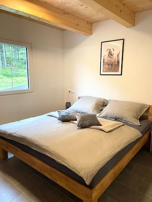 Ein Schlafzimmer mit Holzbett, einem Fenster mit Blick auf Bäume und einem gerahmten Bild an der Wand.