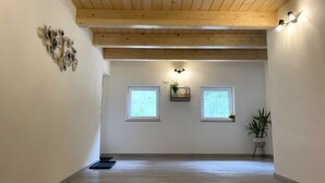 A hallway with wooden beams, two windows, a wall-mounted light fixture, and a potted plant.