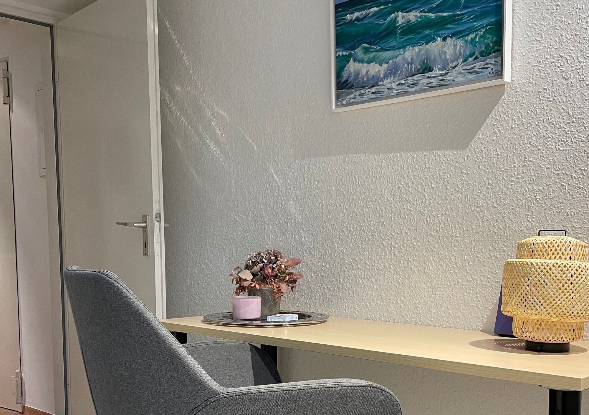 Ein Zimmer mit Schreibtisch, Stuhl, einem Wandbild und einer Lampe.