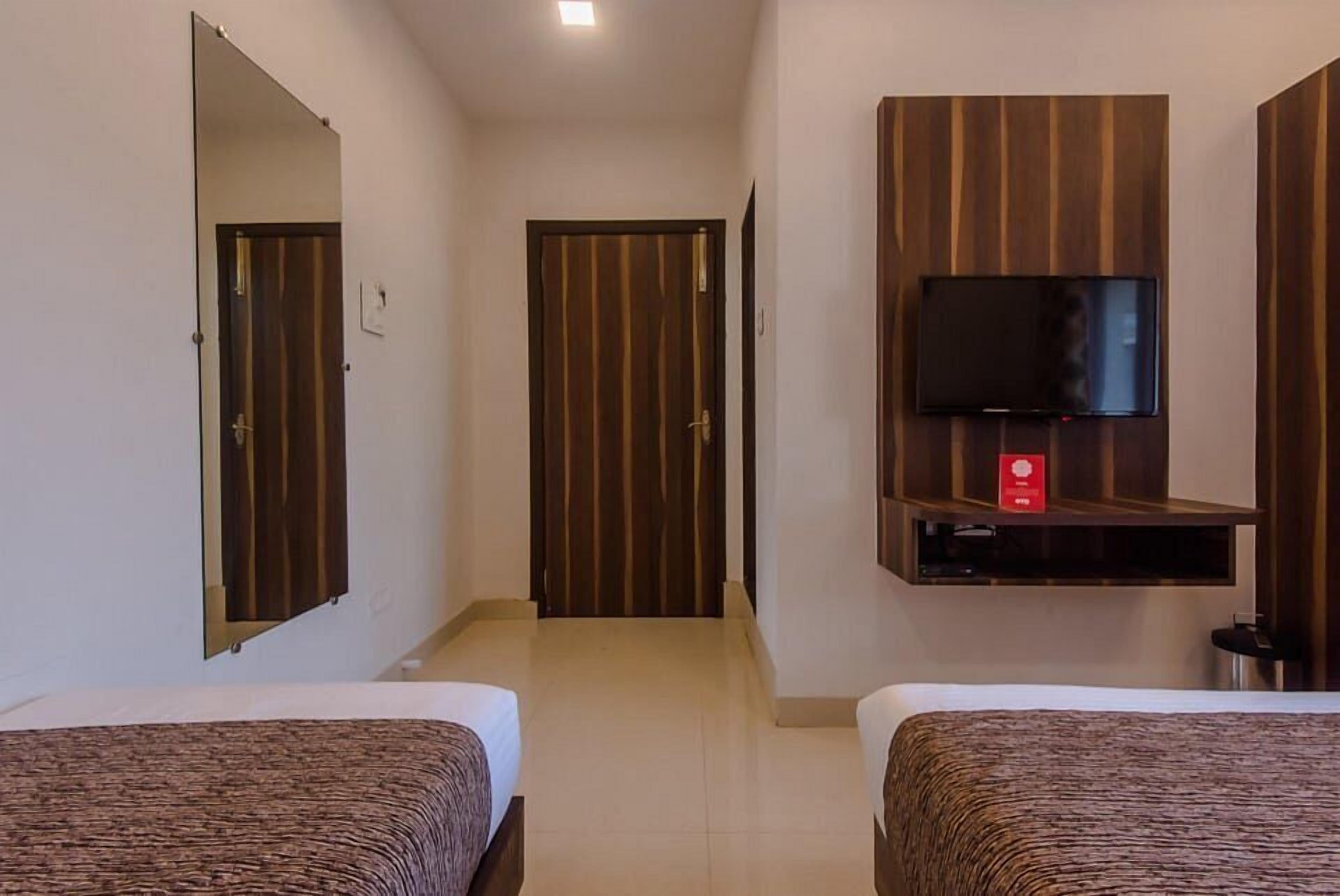 A hotel room with two beds, a TV mounted on a wooden panel, and a mirror on the wall.