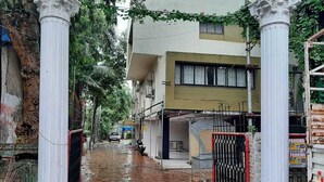 A narrow alleyway with white columns, a gated entrance, and buildings on either side. - Hotel Golden Palms (Mumbai)