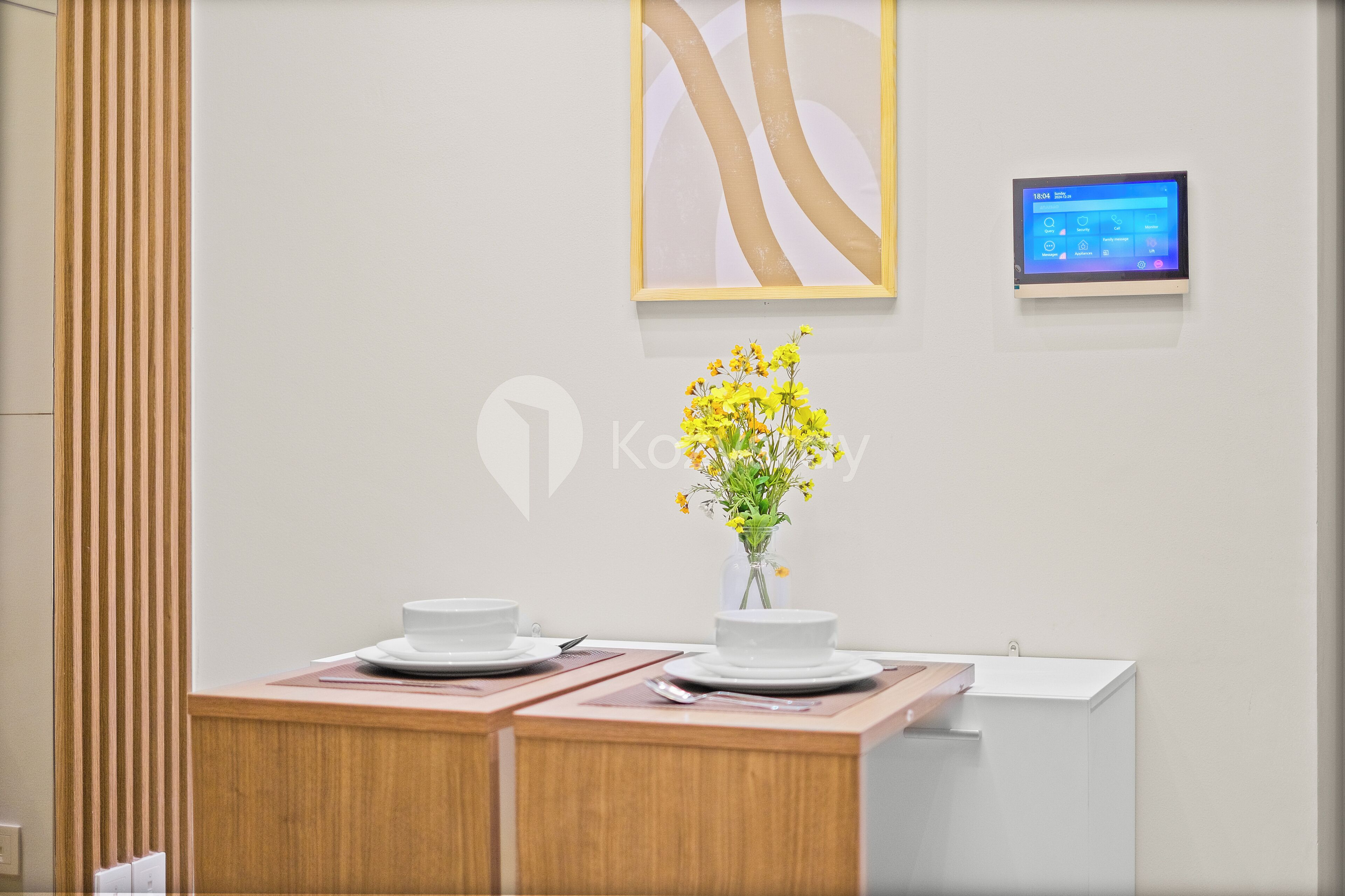 Un área de recepción moderna de hotel con un mostrador de madera, un jarrón de flores amarillas y una pantalla digital en la pared.