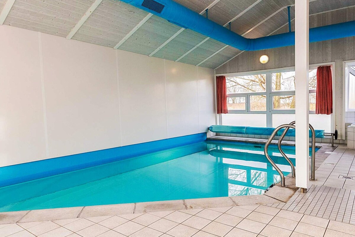 An indoor swimming pool with a blue interior, a tiled floor, and a window with a view of trees.