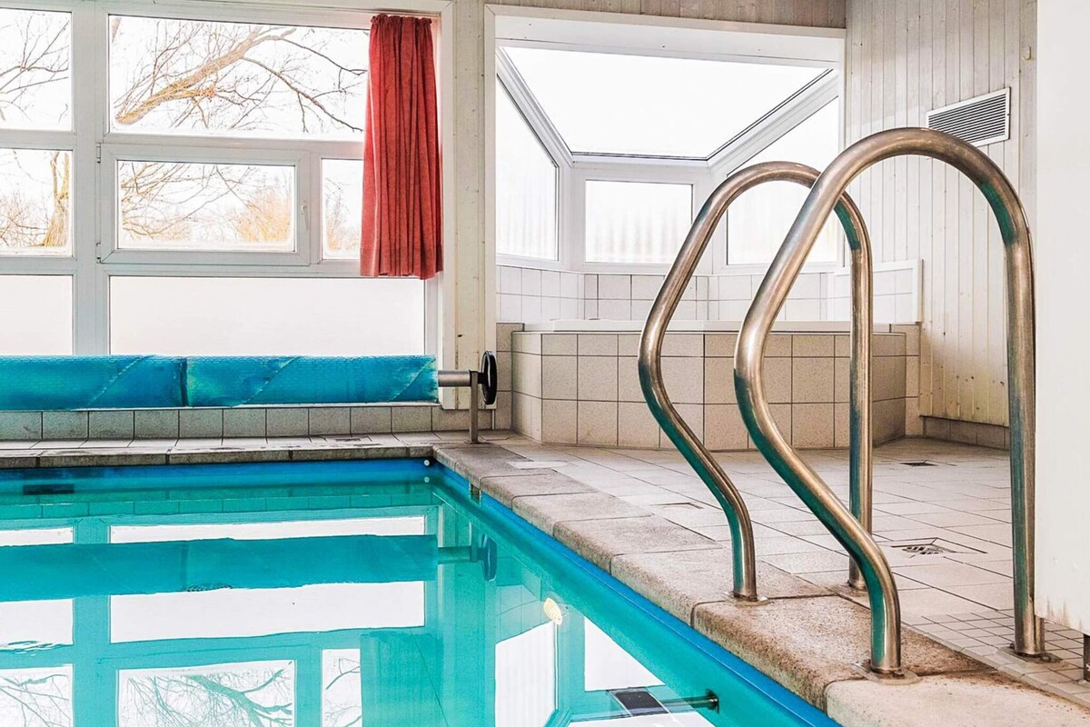 A swimming pool with clear blue water, a blue bench, and a red curtain.