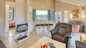 A spacious living area with a wooden interior, a dining table, a leather sofa, and a television. - 4 Star Holiday Home in Ottendorf (Otterndorf)