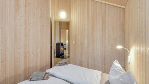 A wooden room with a bed, a wooden wall, a small table with a newspaper, and a fireplace. - 4 Star Holiday Home in Ottendorf (Otterndorf)