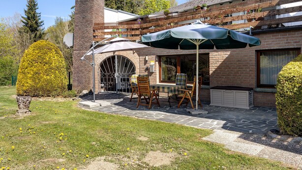 A patio with a table and chairs, a green umbrella, and a brick building with a wooden fence. - Apartment 'Hohenstein' with Mountain View, Private Terrace and Wi-Fi (Willingen (Upland))