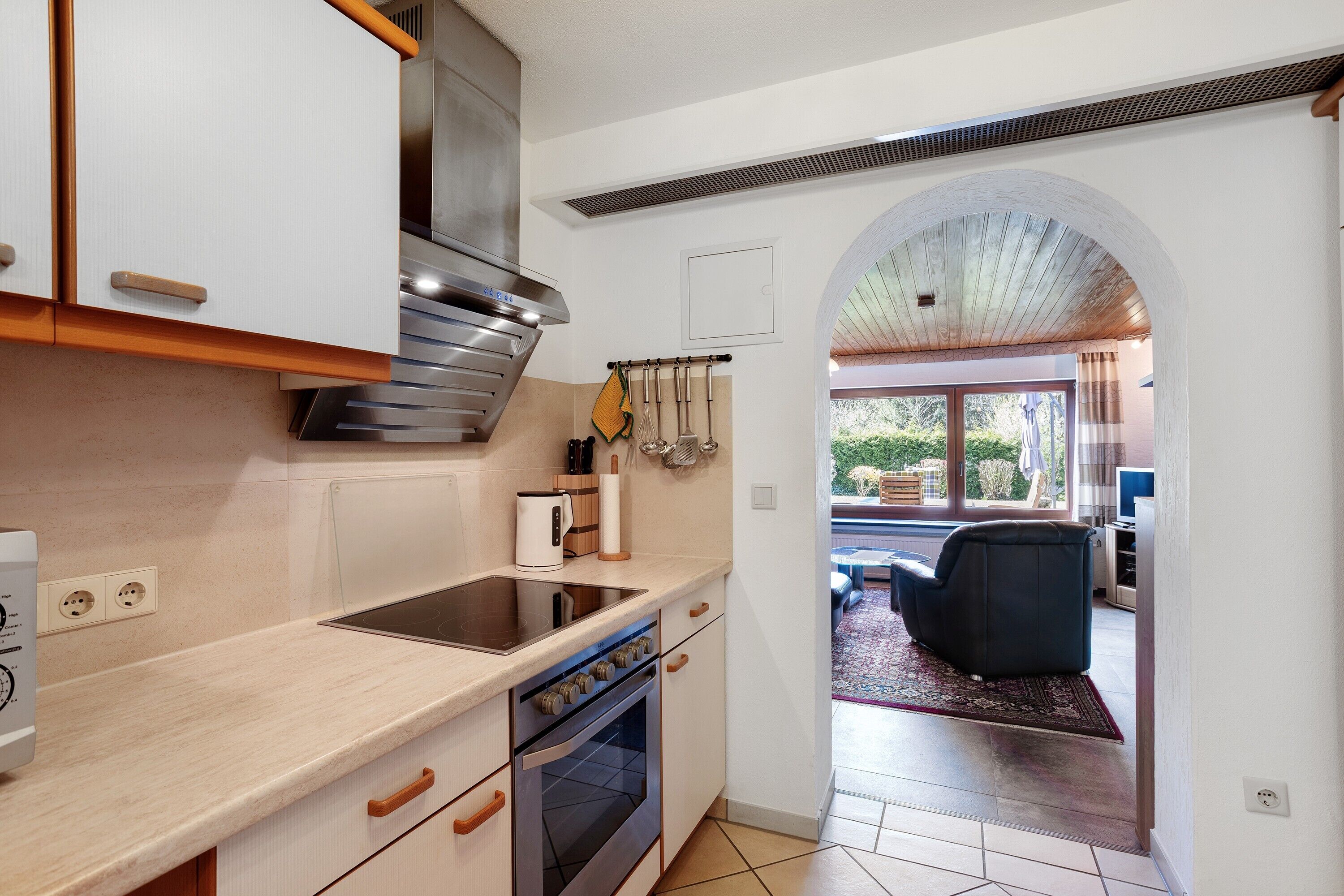 Una cocina con horno integrado, extractor de acero inoxidable y ventana con vistas a un patio.