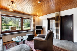 A modern living room with a sofa, ottoman, glass coffee table, and a television. - Apartment 'Hohenstein' with Mountain View, Private Terrace and Wi-Fi (Willingen (Upland))