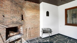 A room with a brick fireplace, a metal grill, a stone floor, and a window with a curtain. - Apartment 'Hohenstein' with Mountain View, Private Terrace and Wi-Fi (Willingen (Upland))