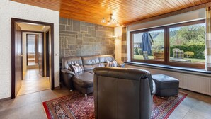 A modern living room with a leather sofa, a wooden ceiling, and a large window with a view of greenery. - Apartment 'Hohenstein' with Mountain View, Private Terrace and Wi-Fi (Willingen (Upland))