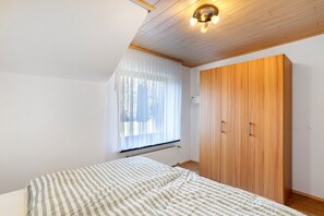 A bedroom with a bed, a wooden wardrobe, a radiator, and a window with curtains. - Apartment 'Hohenstein' with Mountain View, Private Terrace and Wi-Fi (Willingen (Upland))