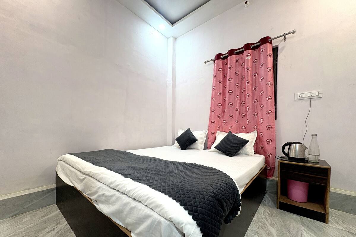 Ein ordentlich eingerichtetes Schlafzimmer mit einem Bett, Kissen, einem Nachttisch mit Wasserkocher und Glas sowie einer Steckdose an der Wand.