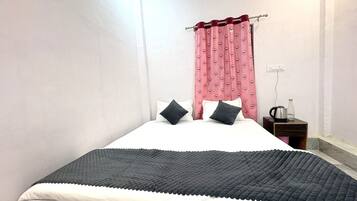 A bedroom with a bed, pillows, a nightstand, a kettle, and a water bottle.