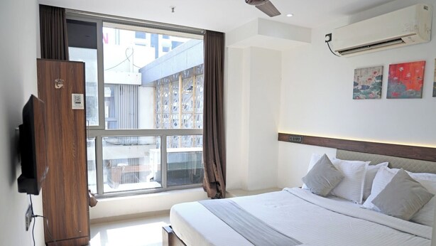 A hotel room with a large bed, a TV, a window with curtains, and artwork on the wall. - Hotel Elegant inn (Surat)