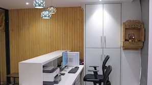 A modern office space with a white desk, black office chair, and a wooden wall. - Hotel Elegant inn (Surat)