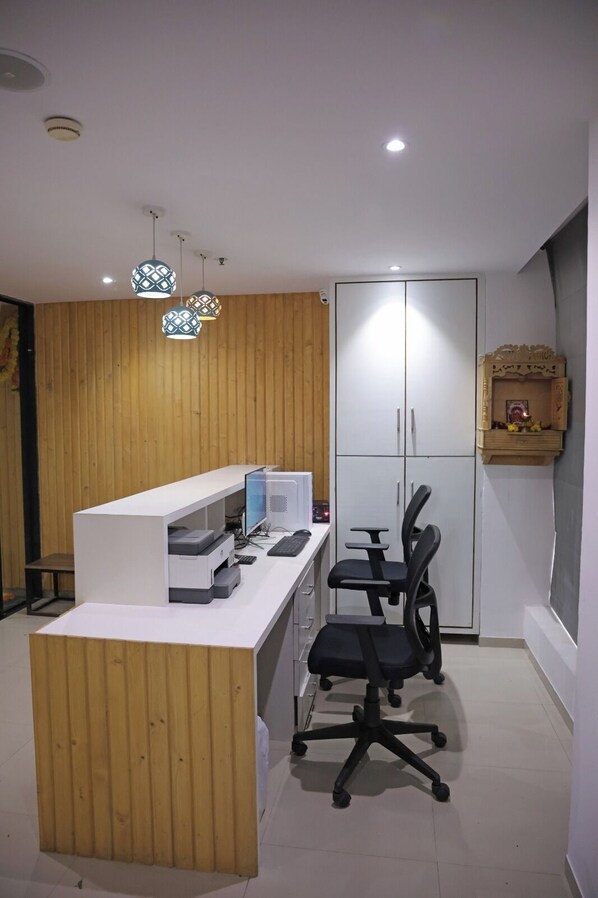 A modern office space with a white desk, black office chair, and a wooden wall. - Hotel Elegant inn (Surat)