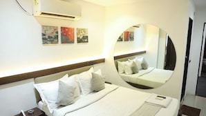 A hotel room with a bed, bedside table, and a wall-mounted air conditioner. - Hotel Elegant inn (Surat)