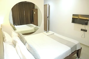 A hotel room with a bed, a round mirror, a TV mounted on the wall, and a door with a number sign. - Hotel Elegant inn (Surat)