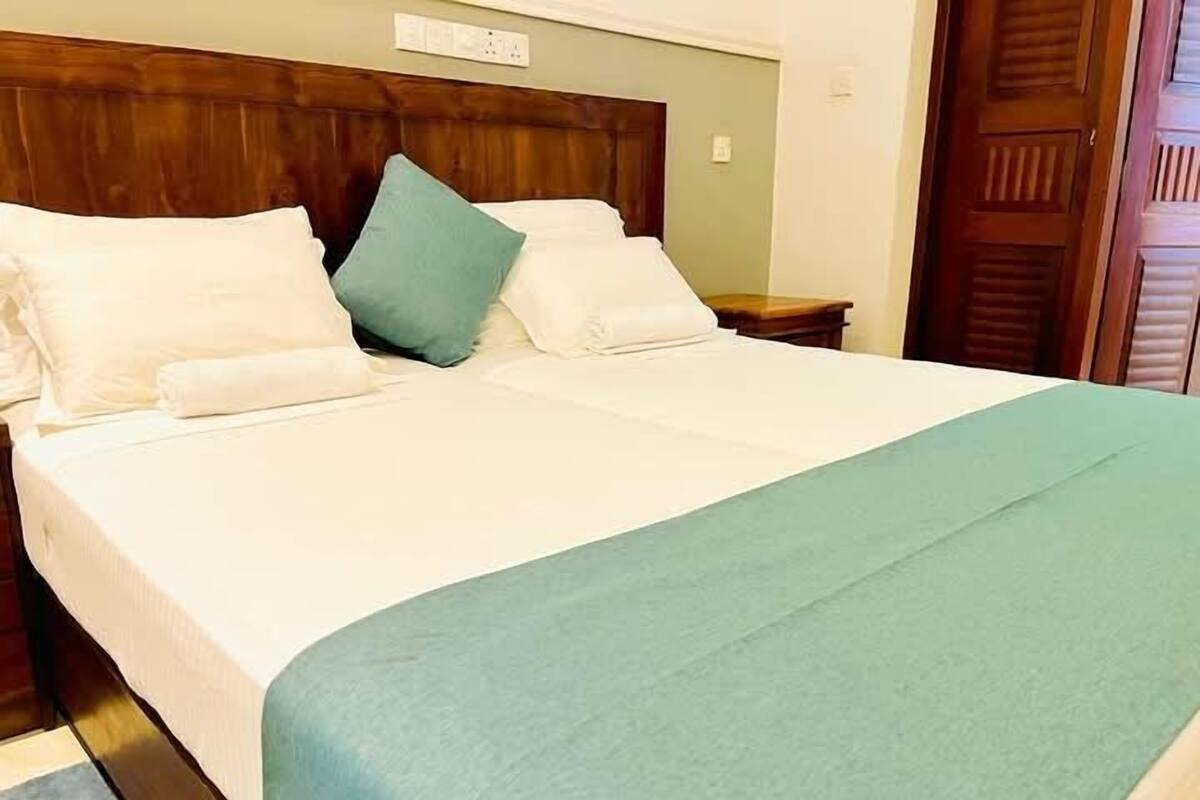 A neatly made bed with white and teal bedding, a wooden headboard, and a wooden nightstand with a lamp.